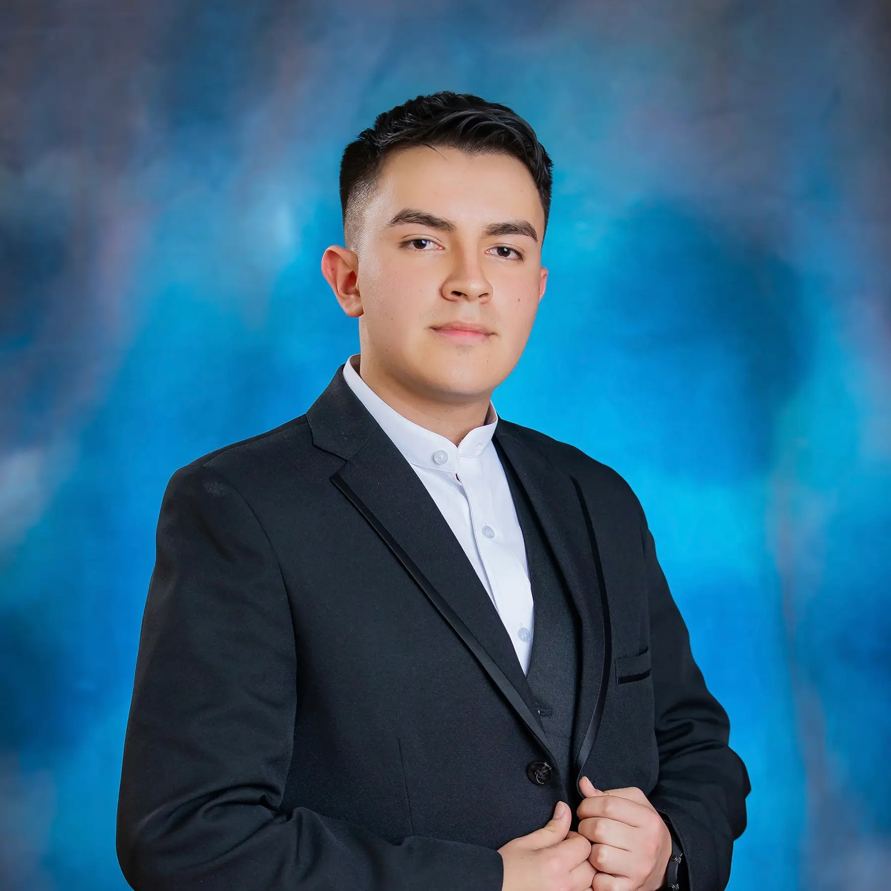 Cristian Ñustes wearing a black suit against a blue studio backdrop